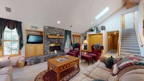 Una sala de estar acogedora con chimenea de piedra, asientos cómodos, televisor y una escalera que sube a otro nivel.