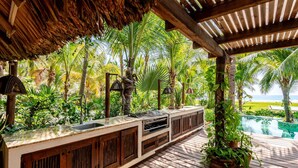 An outdoor bar area with a wooden deck, a thatched roof, and a view of a pool and ocean. - Unique beach house, luxury experience (Puerto Escondido)