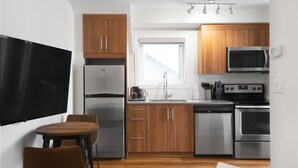 A compact kitchen with wooden cabinets, stainless steel appliances, a built-in oven, and a window providing natural light. - Basecamp Resorts Canmore I Micro-Suite Apartment (Canmore)