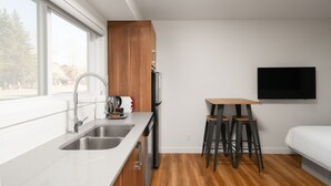 A compact kitchen with a sink, wooden cabinets, and a bar stool. - Basecamp Resorts Canmore I Micro-Suite Apartment (Canmore)