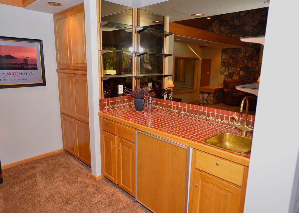 A kitchen with wooden cabinets, a red-tiled backsplash, a gold sink, and a framed picture on the wall.