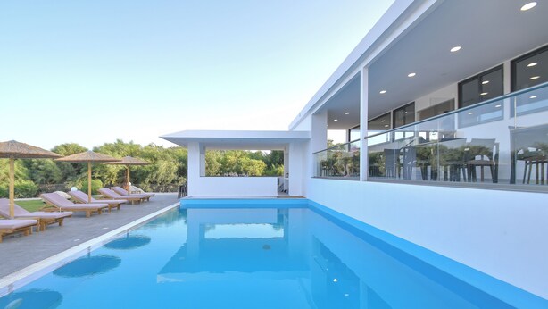 Un espace piscine moderne, doté de chaises longues et de parasols, d’une rambarde en verre et offrant une vue dégagée sur la végétation environnante.