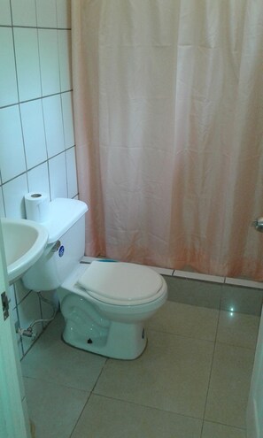 A small bathroom with a toilet, sink, and shower curtain. - Pura Vida Condo (Tamarindo)