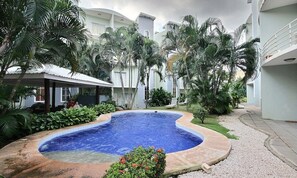 A swimming pool surrounded by palm trees and a covered seating area.