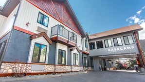 A multi-story building with a "BASECAMP LODGE" sign, stone foundation, and a red roof. - Basecamp Lodge I Micro-Suite Apartment (Canmore)