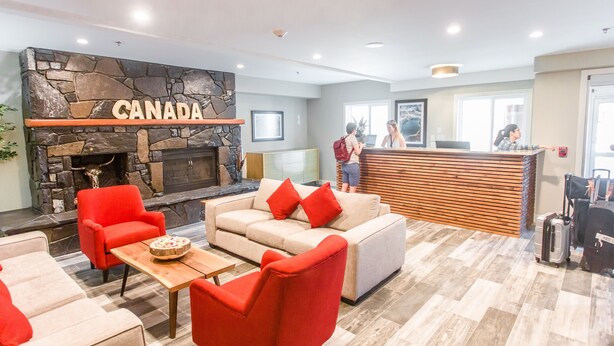 A lobby with a stone fireplace, red and beige sofas, and a reception desk. - Basecamp Lodge I Micro-Suite Apartment (Canmore)