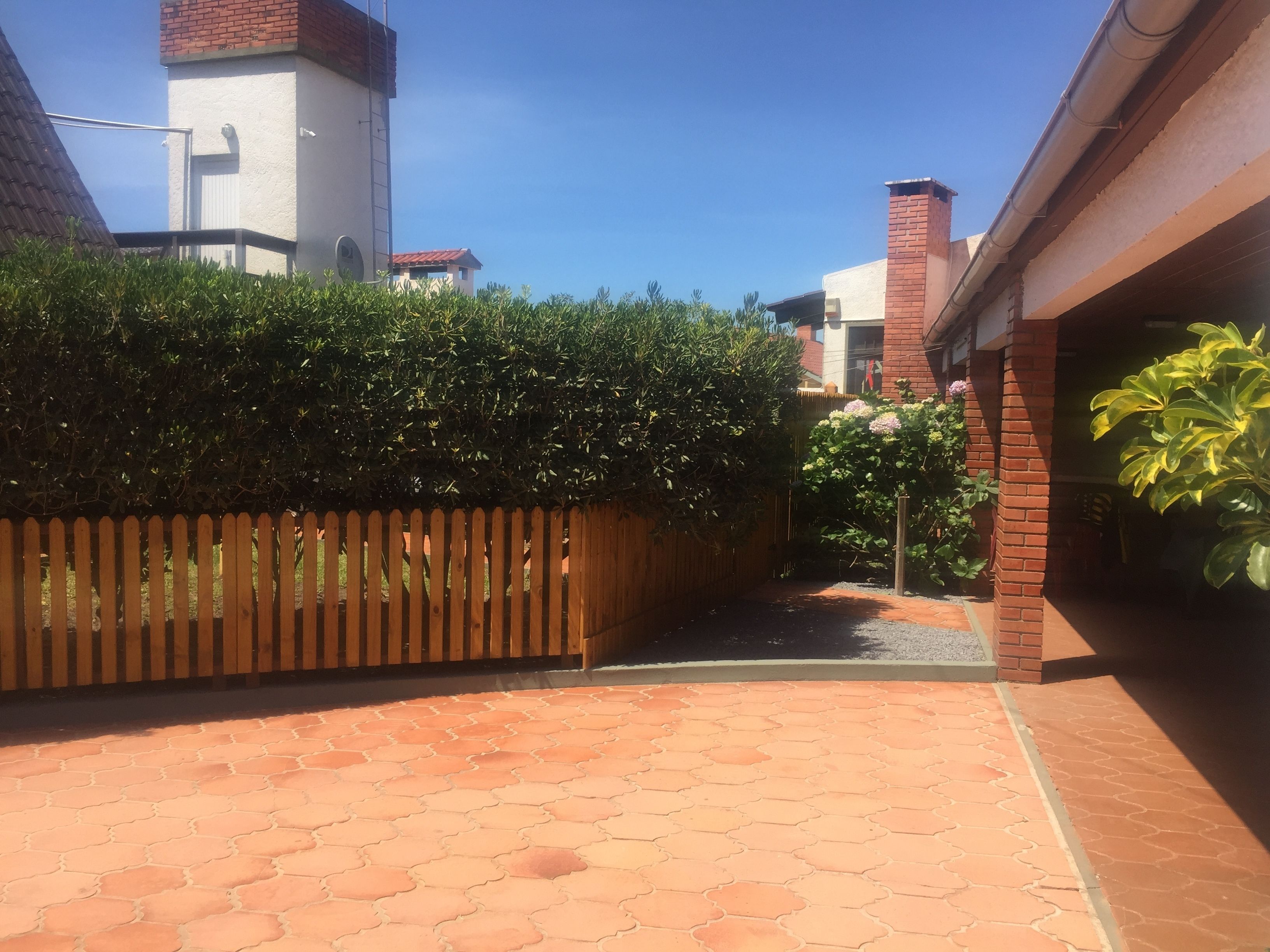 A paved courtyard with a wooden fence, a brick building, and a clear blue sky.
