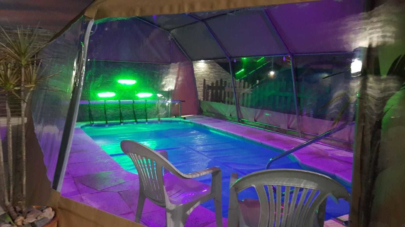 A pool area with a transparent roof, green lighting, and plastic chairs.