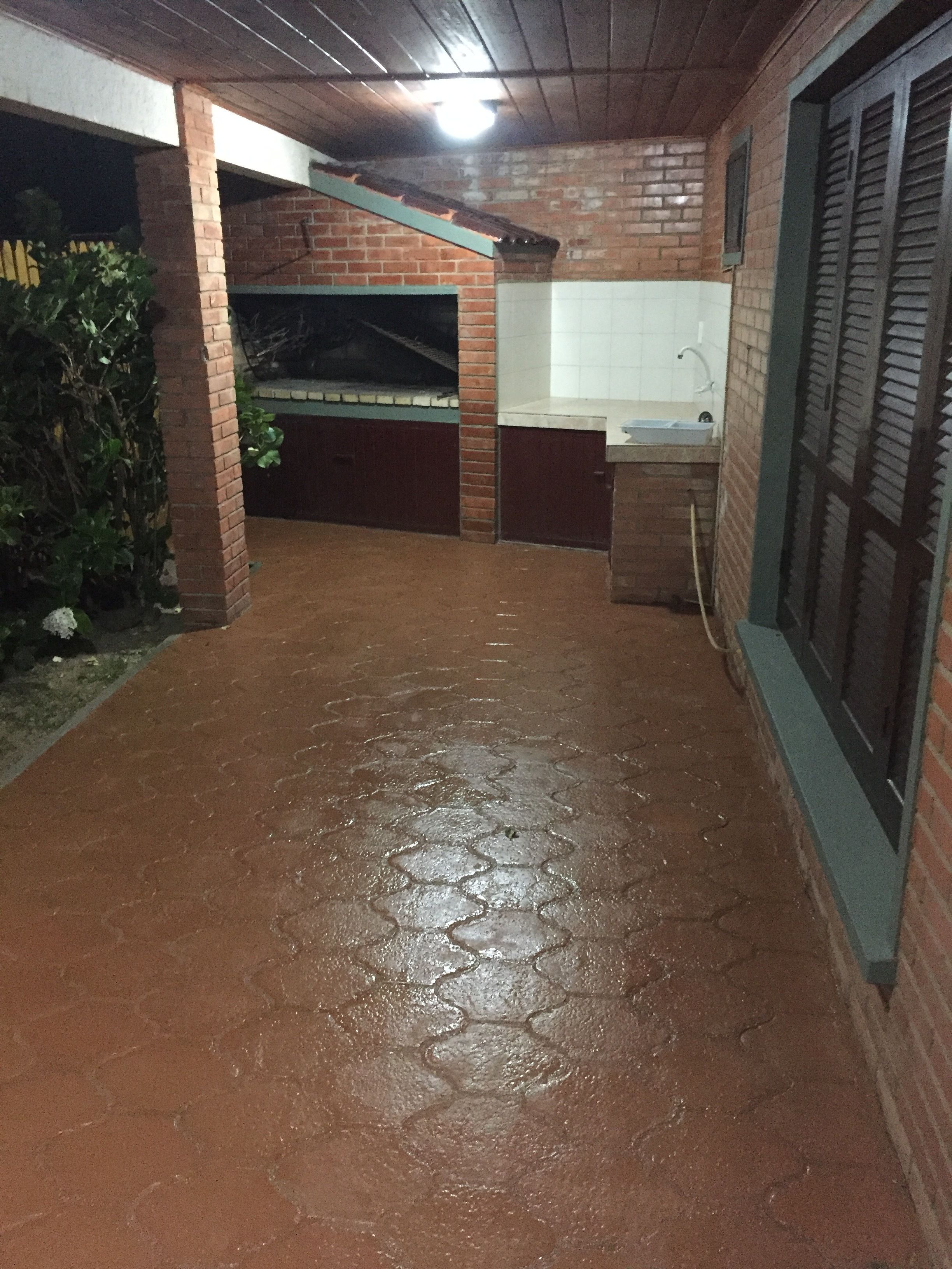 A covered outdoor area with a brick floor, a brick wall, and a window with shutters.