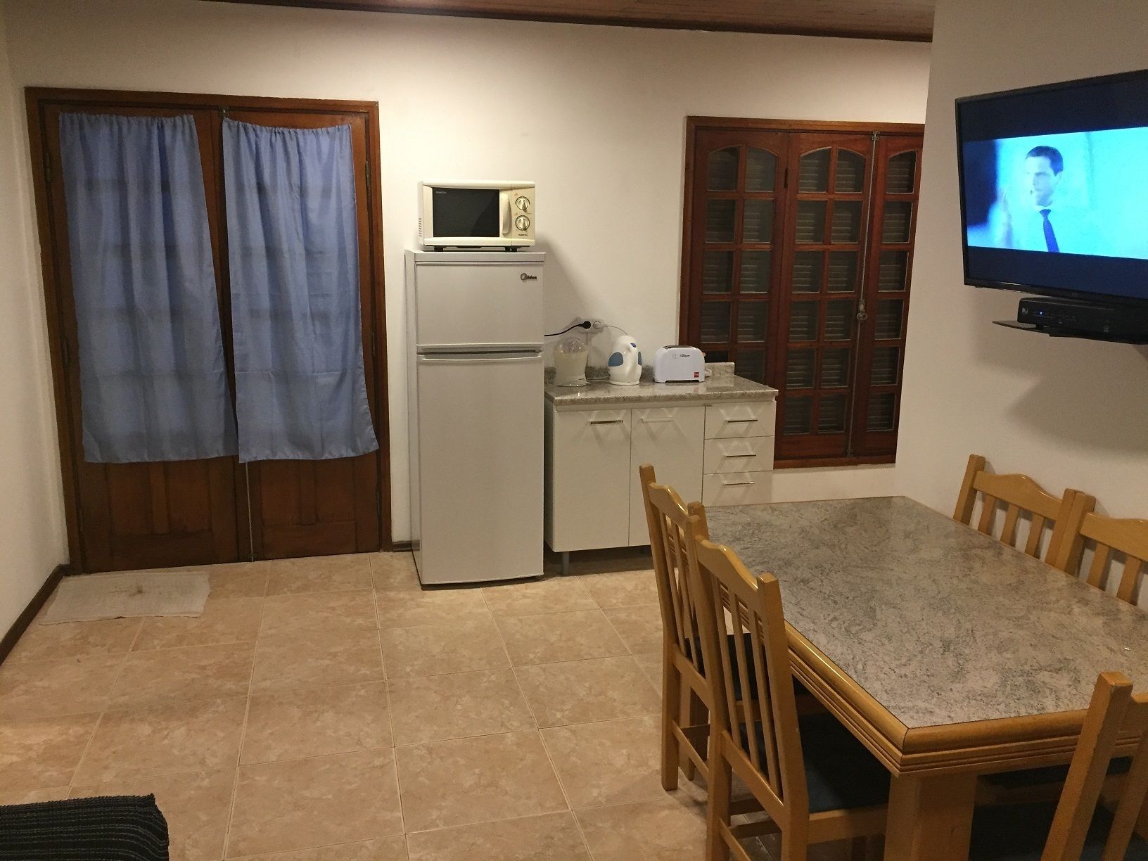 Una cocina compacta con refrigerador, microondas, tostadora y televisión montada en la pared.