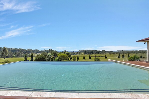 A clear swimming pool with a view of a green landscape and distant hills.