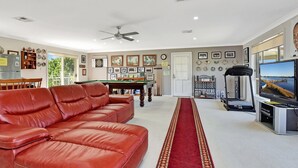 Ein geräumiges Wohnzimmer mit einem roten Ledersofa, einem Billardtisch, einem Fernseher und einem Deckenventilator.