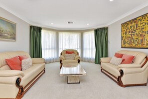Une pièce avec deux canapés en cuir, un fauteuil central, une table basse et des rideaux verts.
