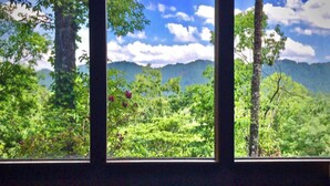A room with a large window overlooking a forested landscape with mountains in the distance. - Mountain Oasis Luxurious w/ 5 Star Amenities! (Bryson City)