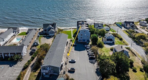 Luchtbeeld van een kustgebied met woningen, een parkeerplaats en een weg naar het strand.