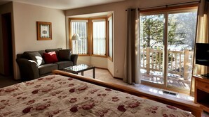 Una camera da letto con un letto, un divano, un tavolino e un balcone affacciato su alberi.