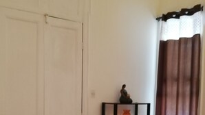 Ein Zimmer mit Holzboden, einer weißen Tür, einem schwarzen Regal mit einer Vase und einem braunen Vorhang.