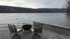 Un patio con dos mecedoras y un hogar para fuego con vistas a un lago.