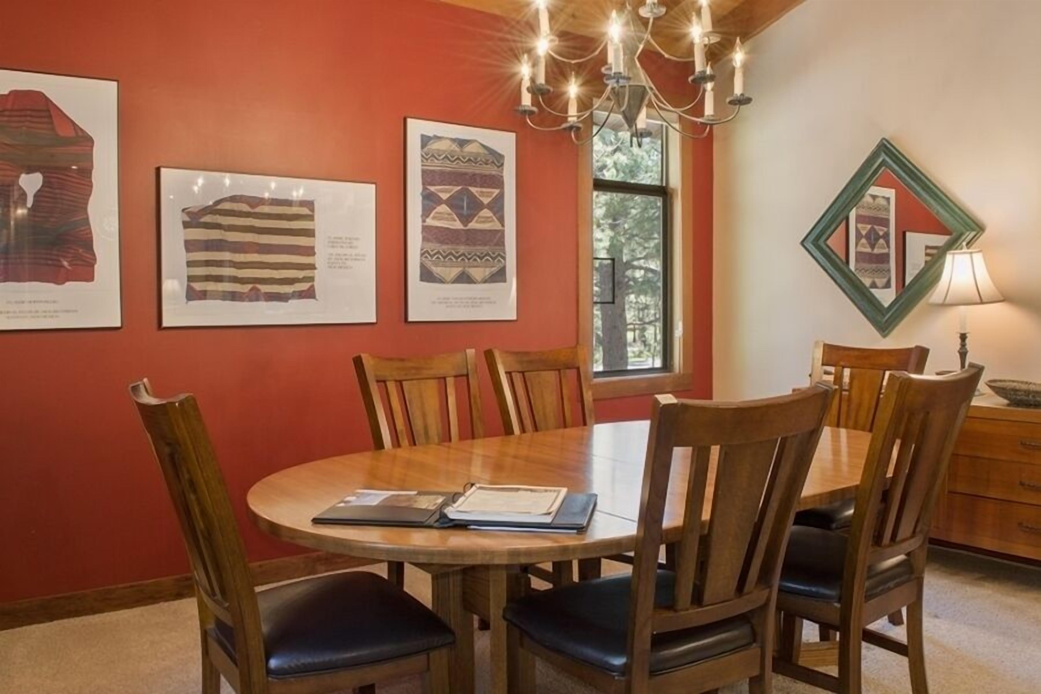 A dining area with a round wooden table, six wooden chairs with black cushions, and three framed textiles on the wall.