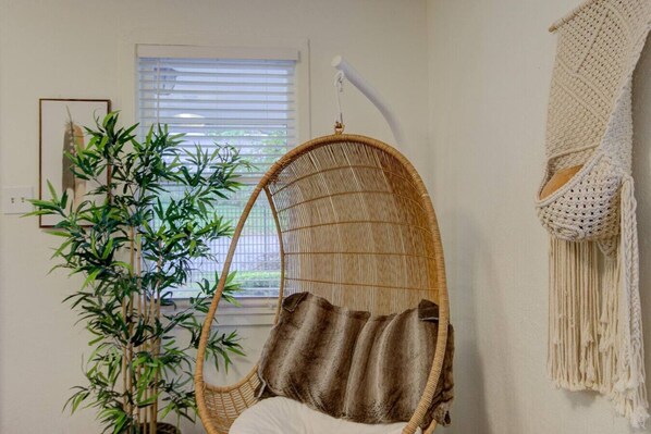 Ein Zimmer mit einem Hängekorbstuhl, einer Wanddekoration aus Makramee und einer Bambuspflanze.