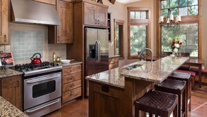 A kitchen with wooden cabinets, a stainless steel refrigerator, granite countertops, and a large island with bar stools. - Lakeside Fun with Access to Forest House (Bend)