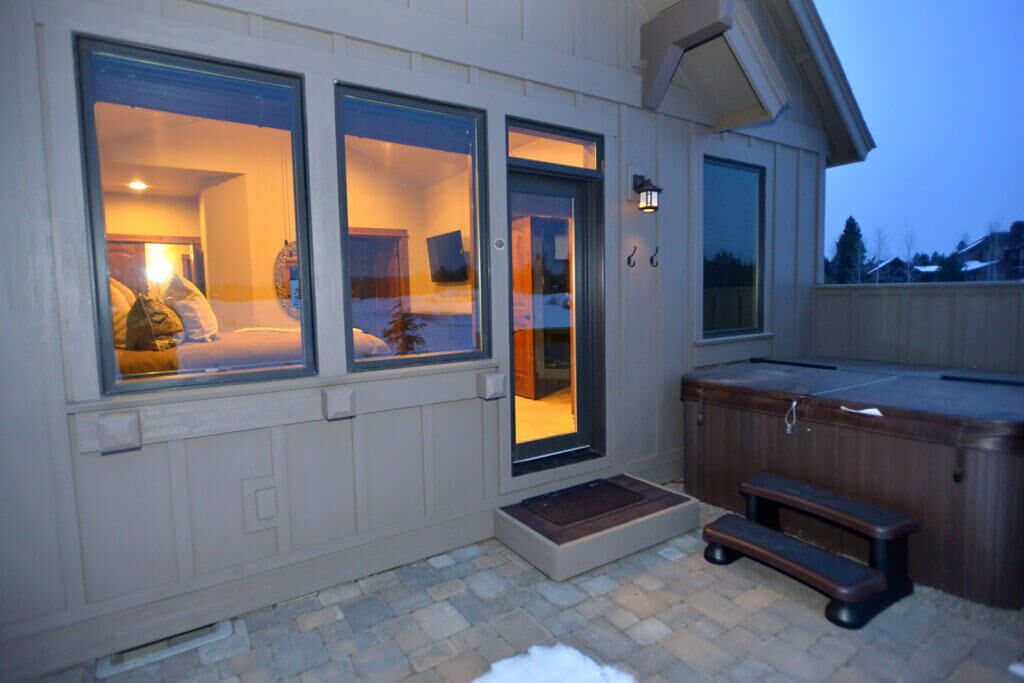 Un espace extérieur accueillant avec un jacuzzi, un banc en bois et une porte-fenêtre coulissante donnant sur une pièce comprenant un lit et une lampe.