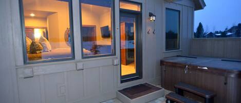 Un espace extérieur accueillant avec un jacuzzi, un banc en bois et une porte-fenêtre coulissante donnant sur une pièce comprenant un lit et une lampe.