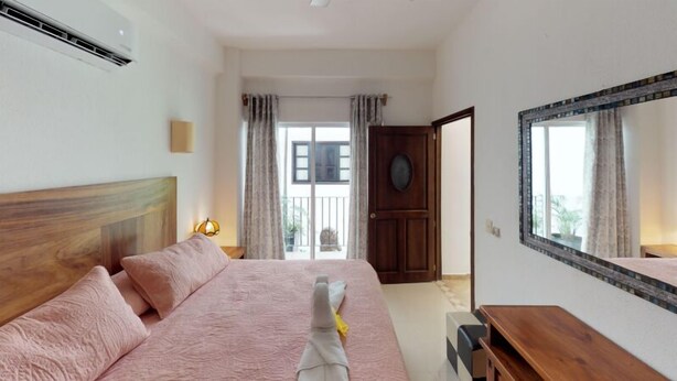 Une chambre à coucher avec un lit, une tête de lit en bois, une table de chevet, un miroir et une vue sur l’extérieur.