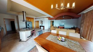 A modern kitchen with a central island, a dining area with a wooden table, and a living space with a sofa and TV. - Andales on the Bay Suites (Puerto Vallarta)