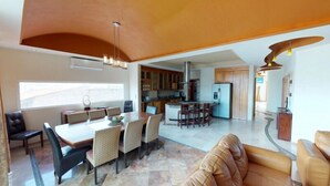 A spacious living area with a dining table, sofas, and a kitchen in the background. - Andales on the Bay Suites (Puerto Vallarta)