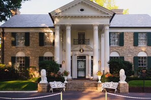 A stately building with a central entrance flanked by columns, a symmetrical facade, and a well-maintained garden with statues and benches. - Cute Midtown Cottage | Steps to Overton & Zoo (Memphis)
