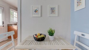 Un comedor con una mesa de madera, sillas blancas, una cesta de frutas y una planta en maceta.