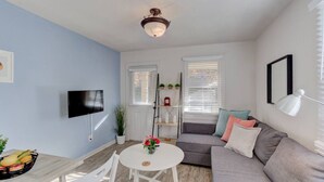 Una sala de estar moderna con un sofá gris, una mesa redonda blanca y un televisor montado en la pared.