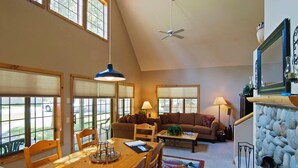 A spacious living room with a high ceiling, a dining area, and a stone fireplace.