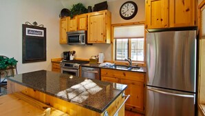 A kitchen with wooden cabinets, stainless steel appliances, a granite countertop, and a clock on the wall.