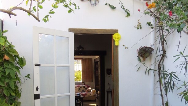 A white door leading to a room with a bed, a table, and a hanging light fixture. - Vila Santíssima - high point of the Historic Center (Tiradentes)