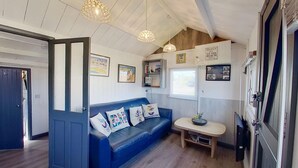 A cozy room with a blue sofa, a small wooden table, and a ceiling with exposed beams. - E19 Roskear, Riviere Towans (Hayle)