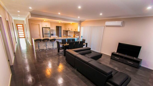 A modern living room with a large black sectional sofa, a flat-screen TV, and a dining area with a bar stool.