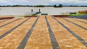 A paved walkway leading to a body of water with a bench and a small island visible in the distance.