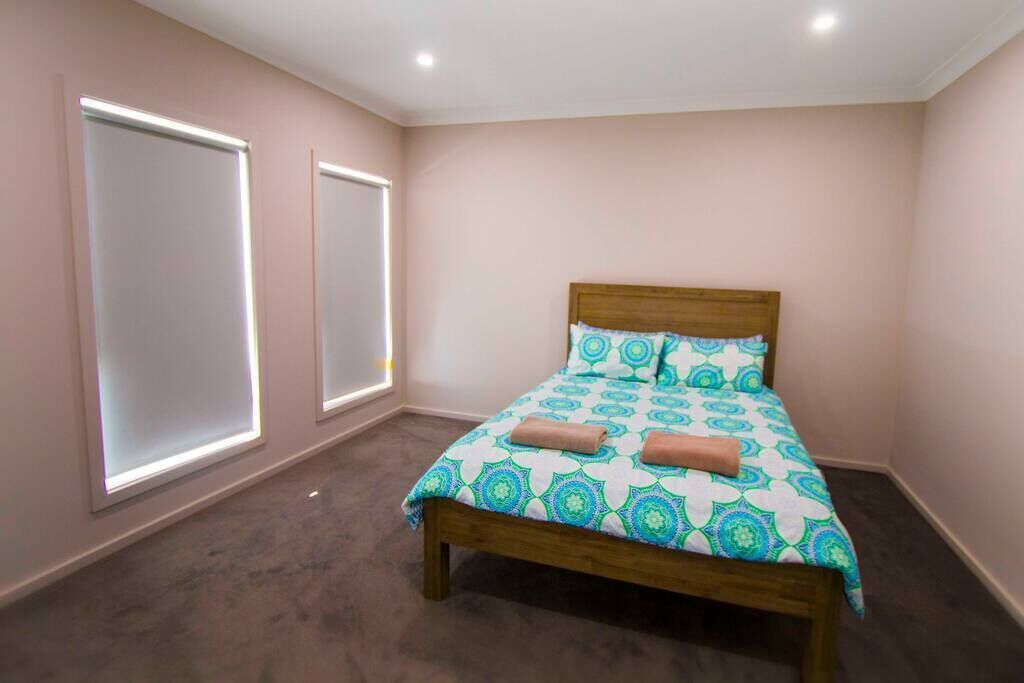 A bedroom with a bed, two windows, and a carpeted floor.