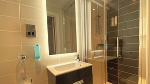 A modern bathroom with a glass shower enclosure, a white sink, and a black vanity. - The Suites- St Pancras Hotel Group (London)