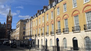 A row of yellow brick buildings with arched windows and a clock tower in the background. - The Suites- St Pancras Hotel Group (London)