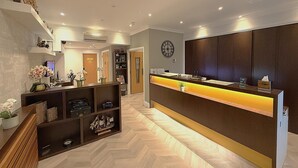 A hotel reception area with a wooden reception desk, a clock on the wall, and a herringbone patterned floor. - The Suites- St Pancras Hotel Group (London)