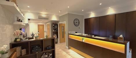 A hotel reception area with a wooden reception desk, a clock on the wall, and a herringbone patterned floor.