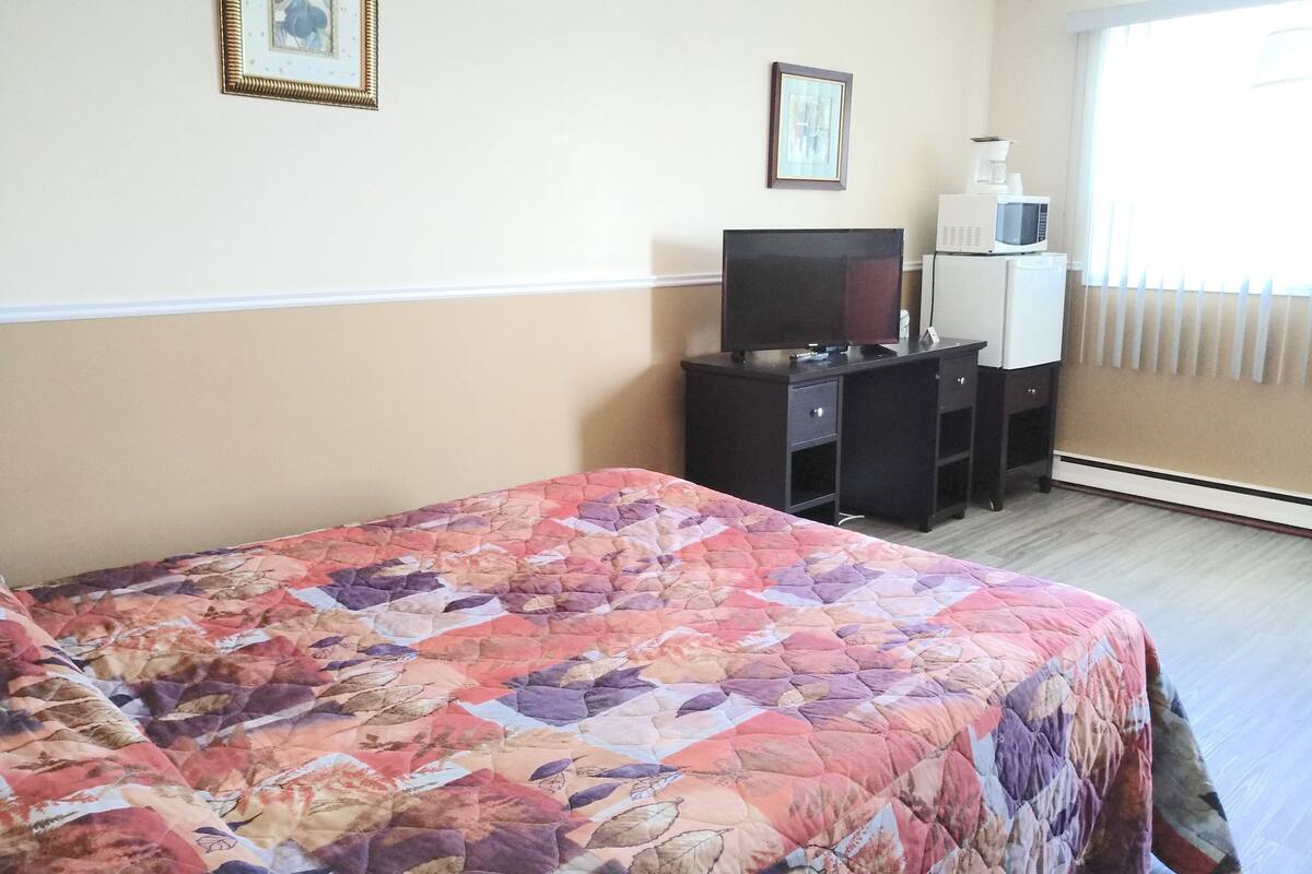 A hotel room with a bed, a desk with a television, a microwave, and framed pictures on the wall.