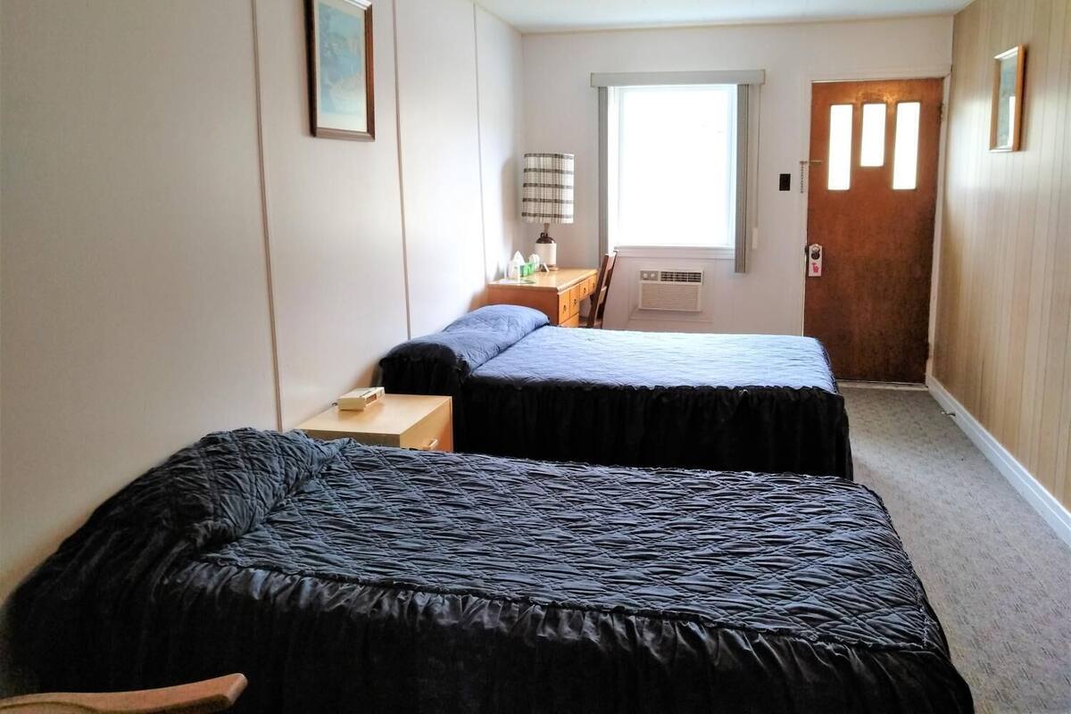 A room with two beds, a small table, a chair, a window, and a door.