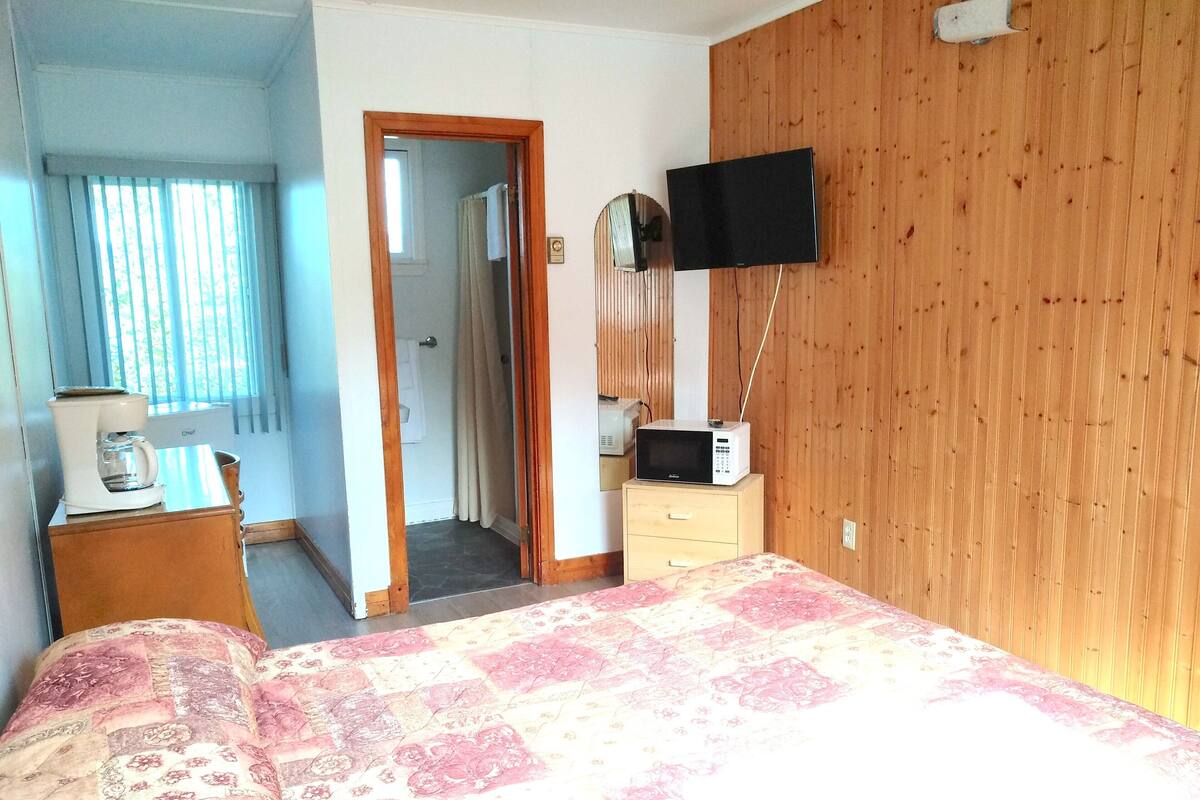 A hotel room with a bed, a wooden wardrobe, a flat-screen TV, a coffee maker, and a bathroom visible through an open door.