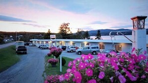 A motel with multiple rooms, a parking lot, and a mountainous backdrop. - Motel Fort Ramsay (Gaspe)