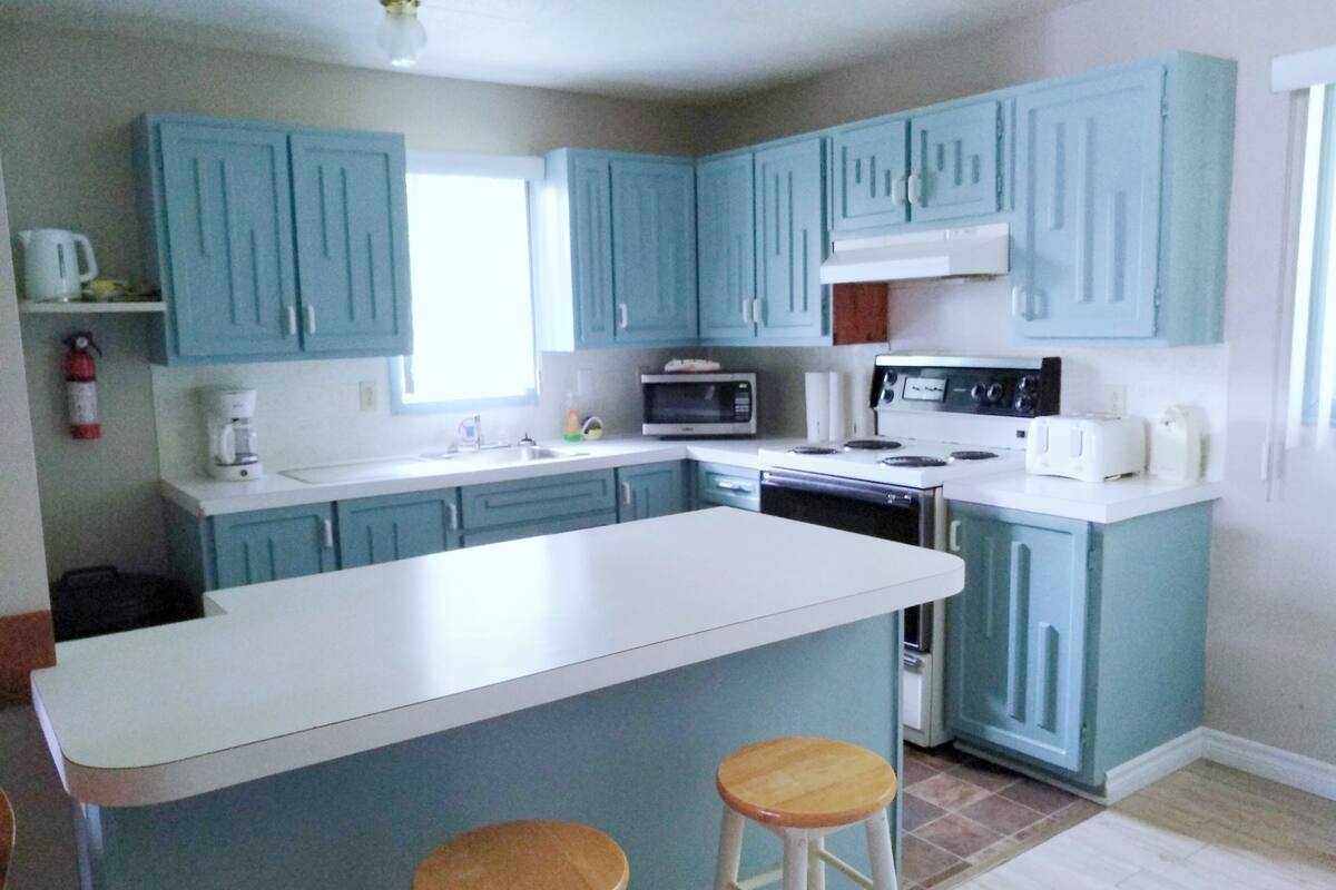 A kitchen with blue cabinets, a white island, and two stools.