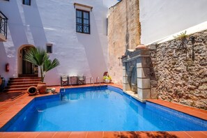 Une piscine bordée d’un mur en pierre et un bâtiment blanc doté d’une porte et de fenêtres.